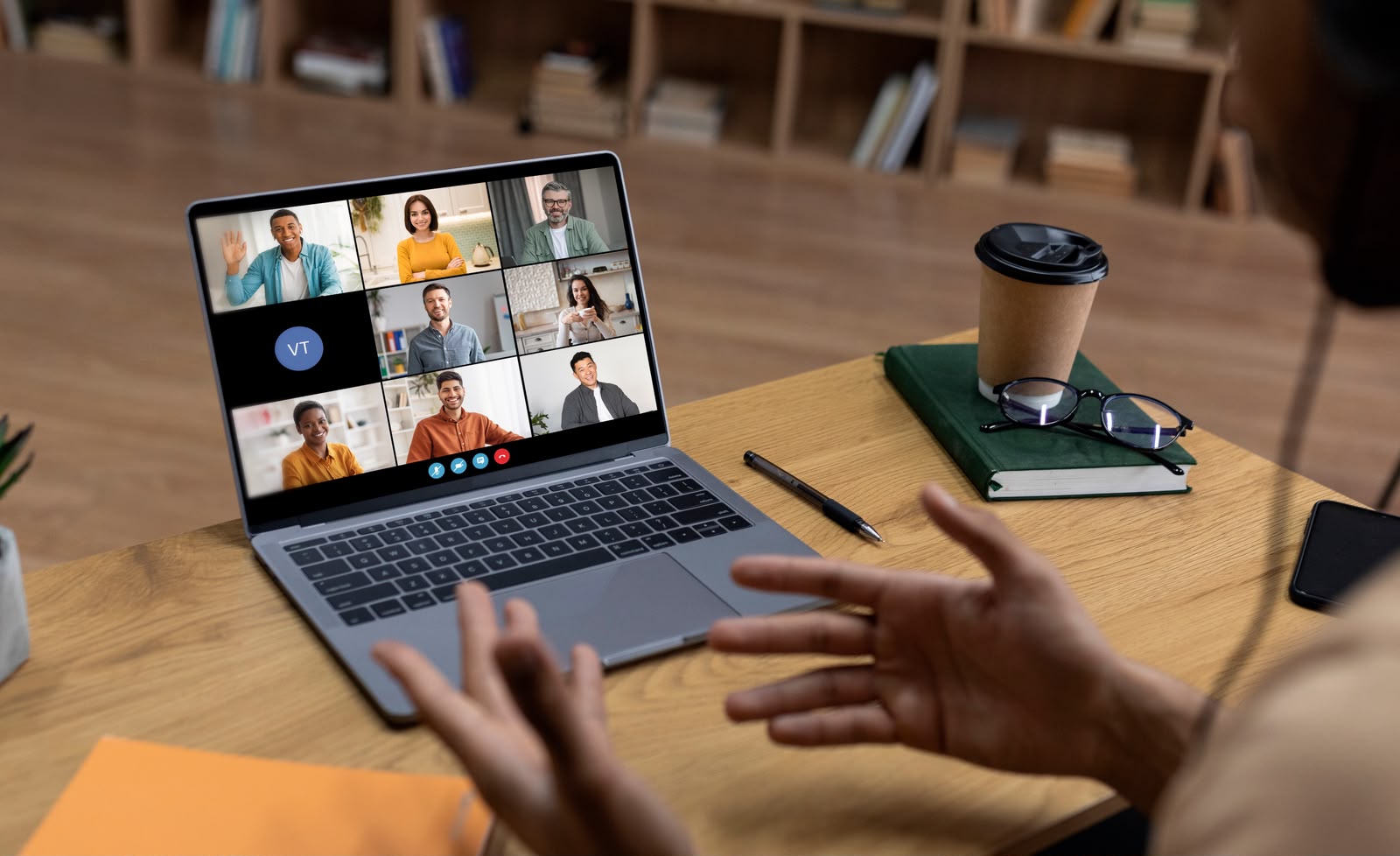 Professional coordinating a multi-person video call from a desk with notebook and coffee